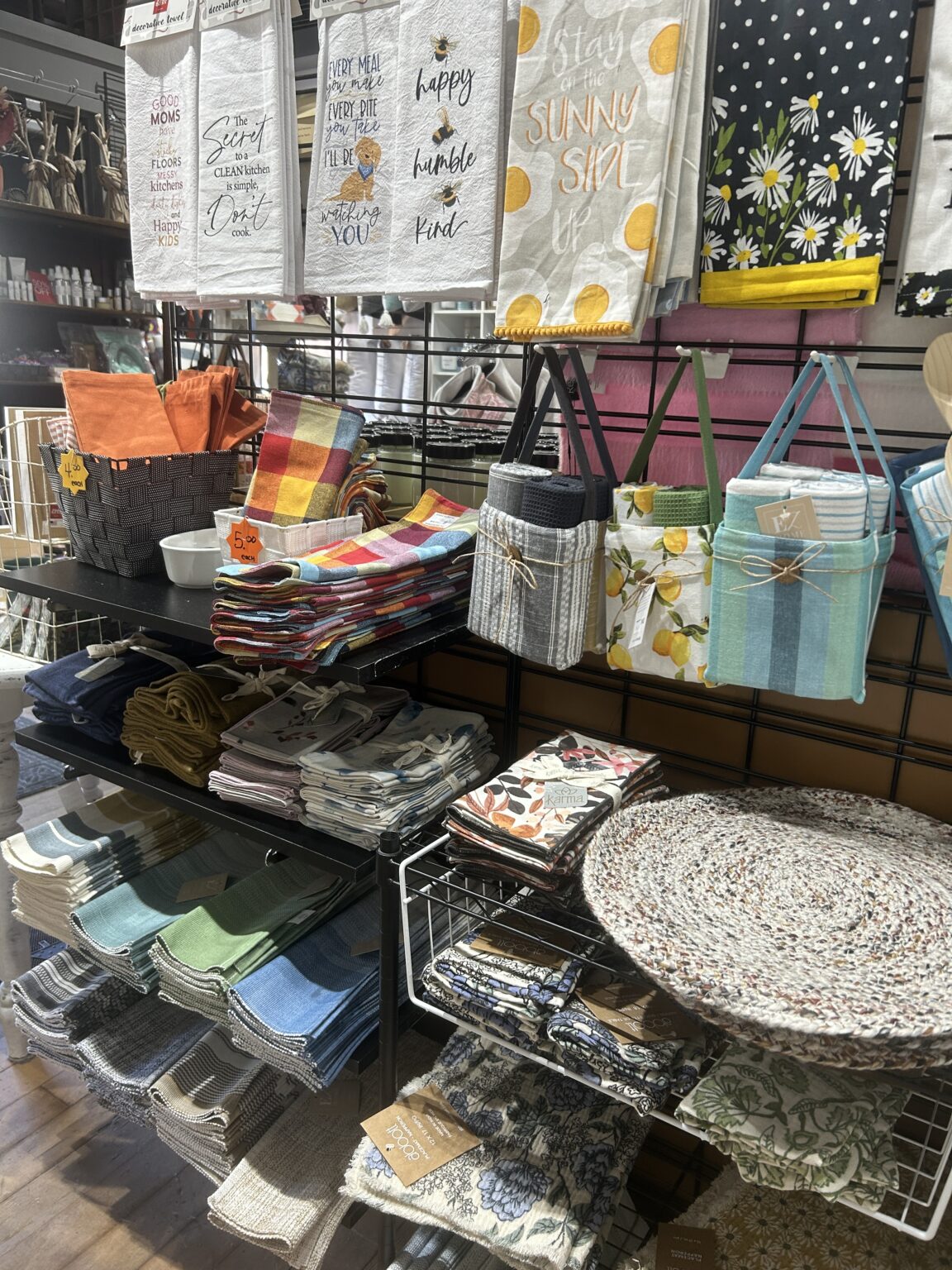 Overhead view of folded multi-colored patterned tea towels, kitchen textiles, and hanging tote bags.