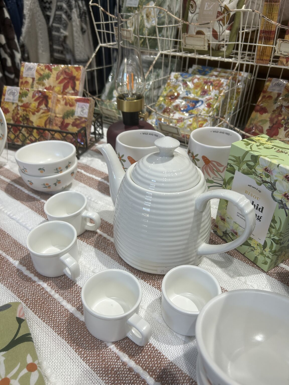 Classic white ceramic teapot surrounded by matching teacups on a retail display table.