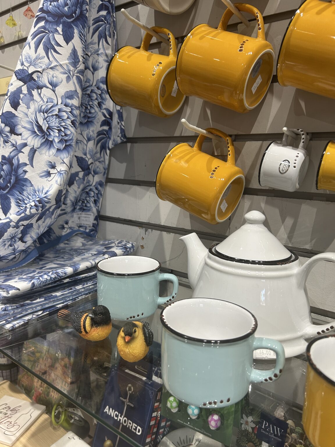 White ceramic teapot accented with bright yellow mugs and saucers on a display shelf.